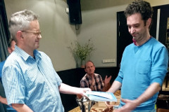Competitieleider Geert Hovens overhandigt Maarten Strijbos een schaakboek als extra prijs. De beker voor het clubkampioenschap staat op tafel