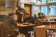 KNSB 22 april 2023. De laatste 4 spelers: Bord 5 Philipp Welzel tegen Peter Wilschut (met pet) en bord 4 Thijmen Smith tegen Rosa Ratsma. Joep Nabuurs en Christian Busch kijken toe.